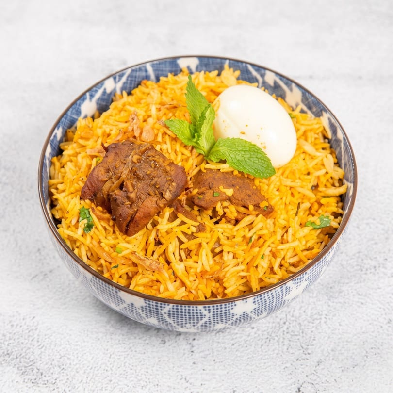 Chicken biryani with a hard-boiled egg and mint garnish in a blue and white patterned bowl.