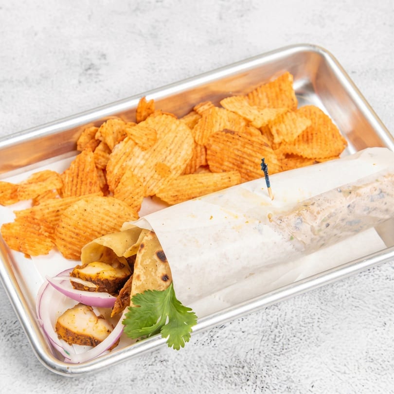 Chicken wrap with red onions and cilantro, served with ruffled potato chips on a metal tray.
