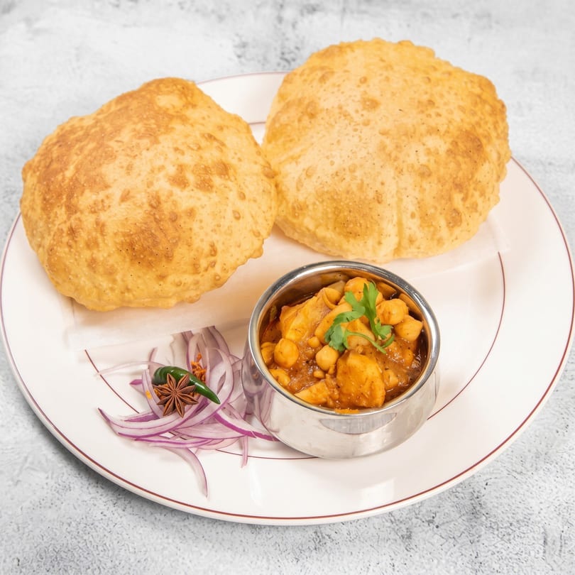 Two golden-brown fried puri breads with a side of chana masala, red onions, and spices.